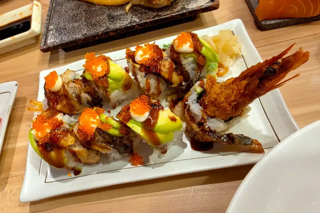 A plate of creative fusion sushi rolls topped with fish roe, avocado, and a crispy fried shrimp tail from The Sushi Bar at Ngee Ann City.