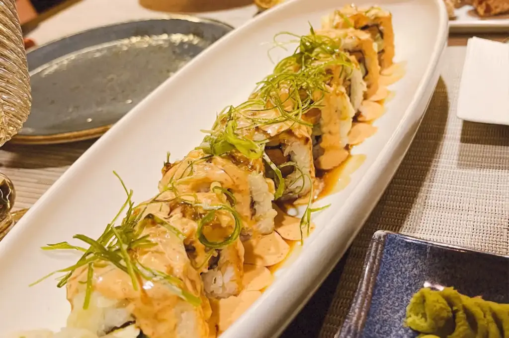 An elongated white plate showcasing signature sushi rolls drizzled with savory sauce and garnished with fresh scallions at sen-ryo, ION Orchard.