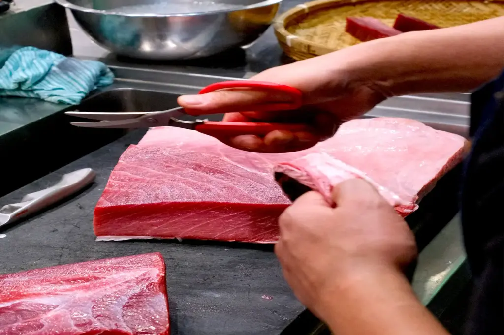 A chef from Araya Shouten carefully preparing and trimming a fresh block of premium tuna sashimi for a Chirashi don.