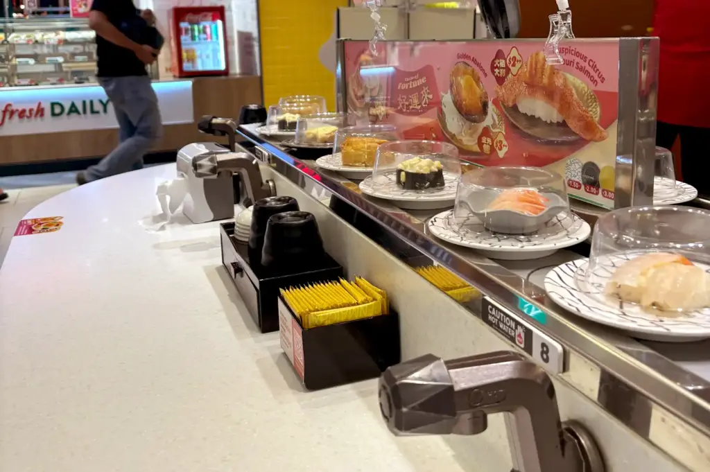 A conveyor belt overflowing with various plates of affordable sushi covered with protective domes at a Sushi Express outlet.