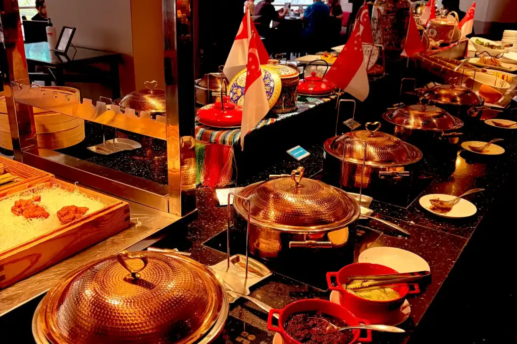 A halal buffet line featuring polished copper chaffing dishes, red condiment bowls, and miniature Singapore flags set against a dark countertop.