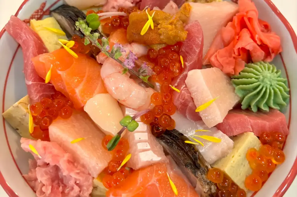 A close-up, beautifully arranged bowl of classic Japanese Chirashi don overflowing with thick cuts of raw salmon, tuna, creamy sea urchin, and glittering ikura.