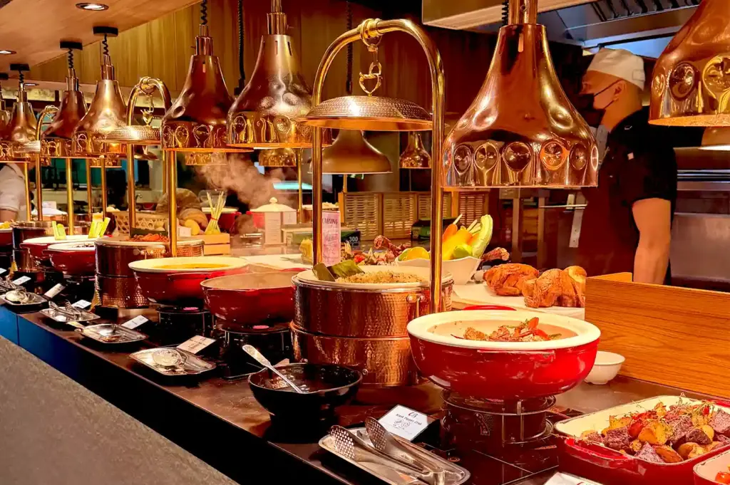A fully stocked buffet station with copper heat lamps, large red pots, roasted whole chickens, and prepared hot dishes ready for guests.