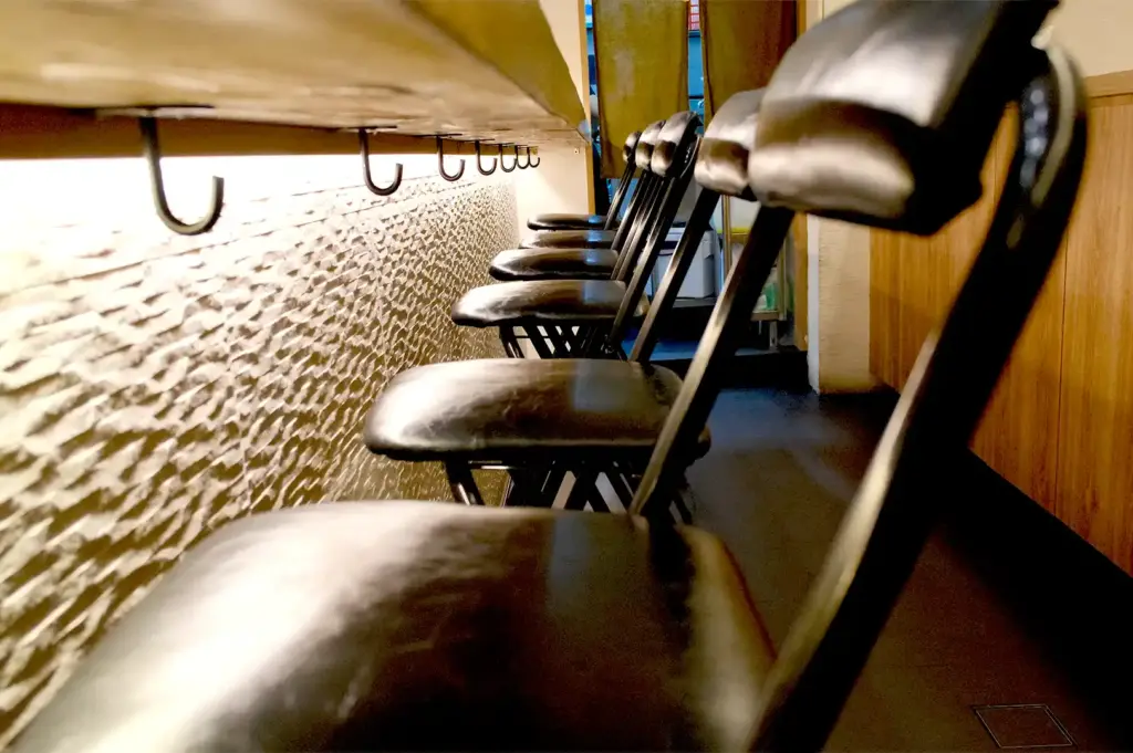 A row of sleek black leather bar stools neatly aligned along the wooden counter of Sushi To Sumi, emphasizing the restaurant's intimate omakase dining setup.