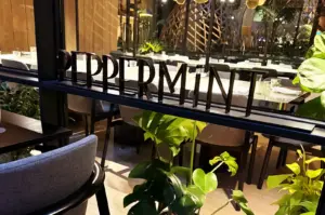 Black dimensional lettering spelling PEPPERMINT on a glass partition surrounded by lush indoor greenery inside PARKROYAL COLLECTION Marina Bay.