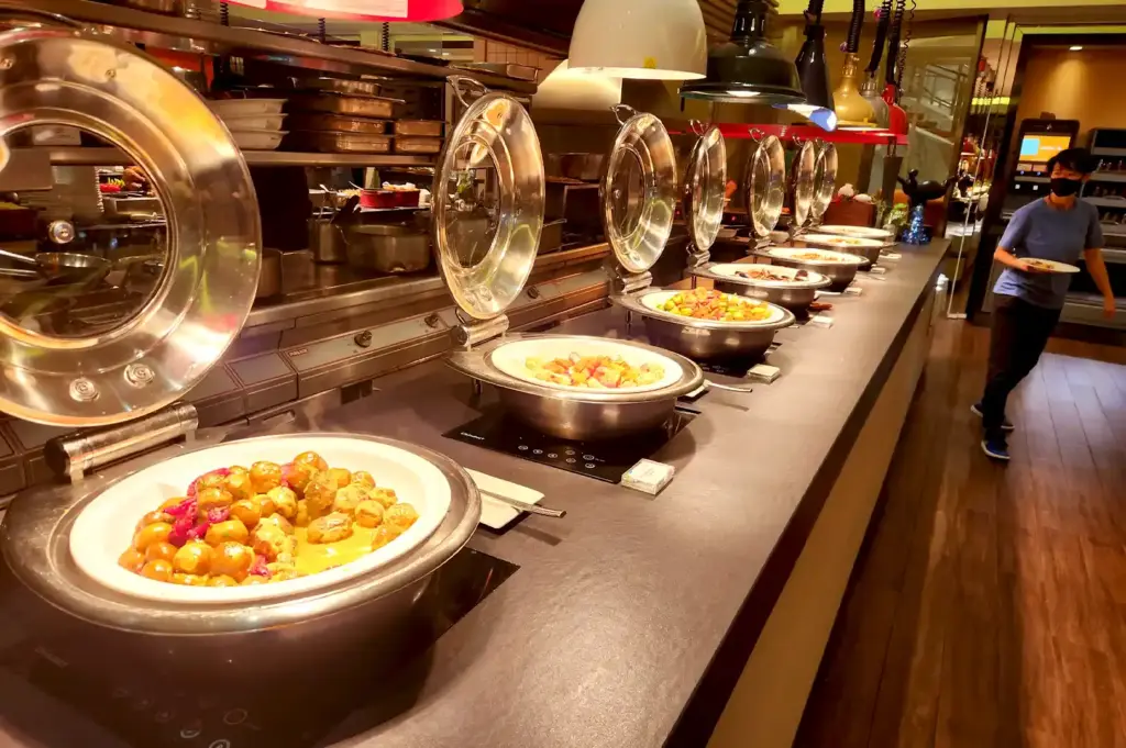 Long buffet counter line featuring hot international dishes in stainless steel chafing dishes at Carousel Buffet.