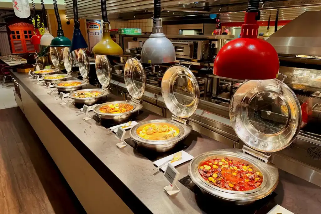 Array of heated buffet stations with overhead heat lamps displaying hot mains at Carousel Buffet.