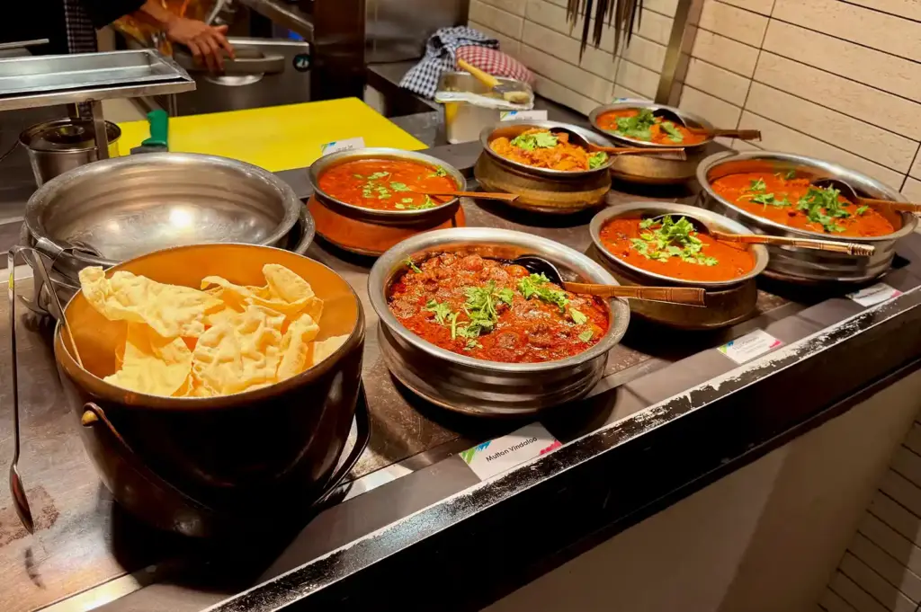 Indian food station at Carousel Buffet showcasing pots of rich curries, mutton vindaloo, and crispy papadums.