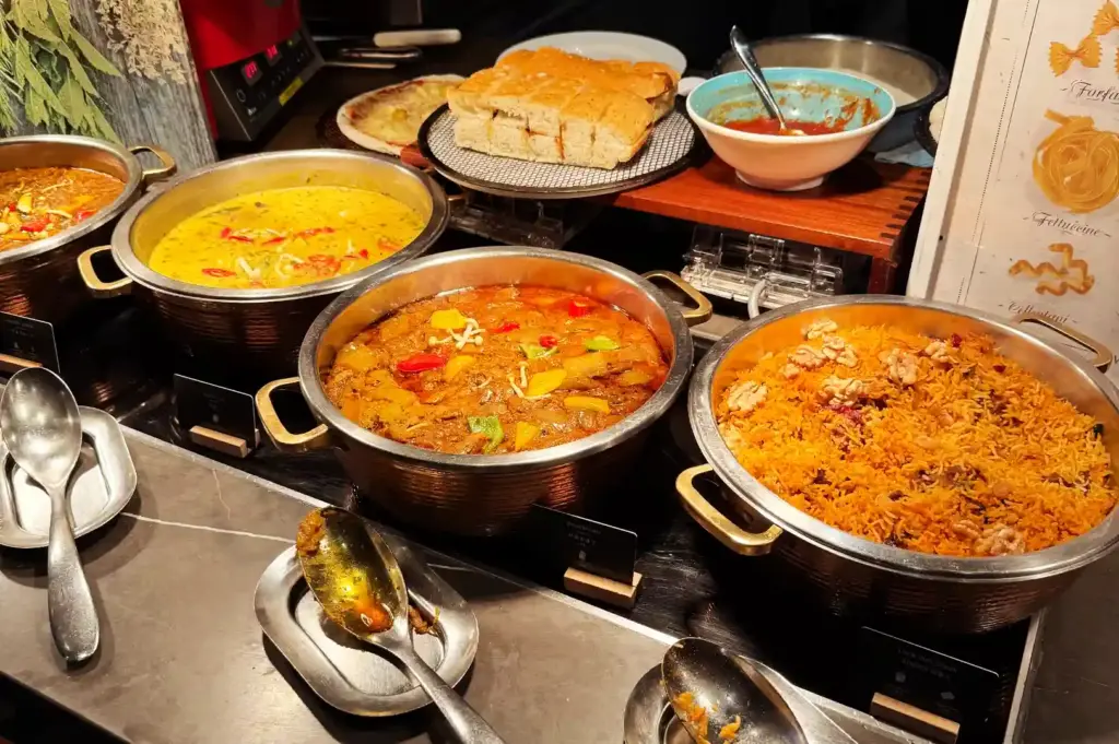 A line of stainless steel chafing pots presenting hot buffet curries, stews, and biryani rice topped with walnuts at Peppermint.
