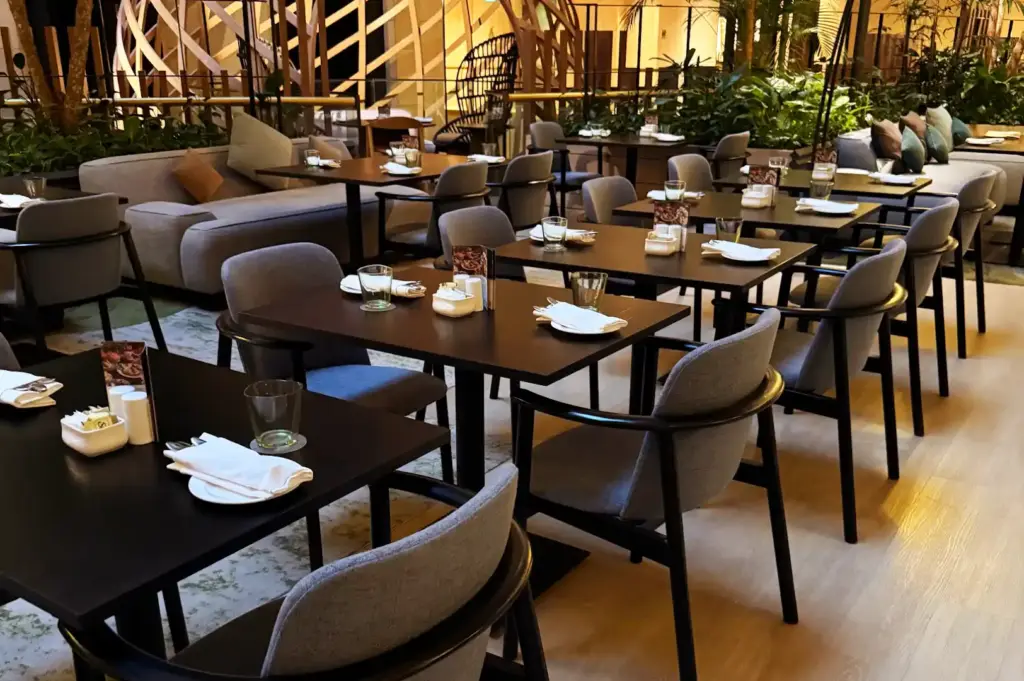 Modern and serene restaurant seating area at Peppermint with dark wood tables, upholstered grey chairs, sofa seating, and indoor garden elements.
